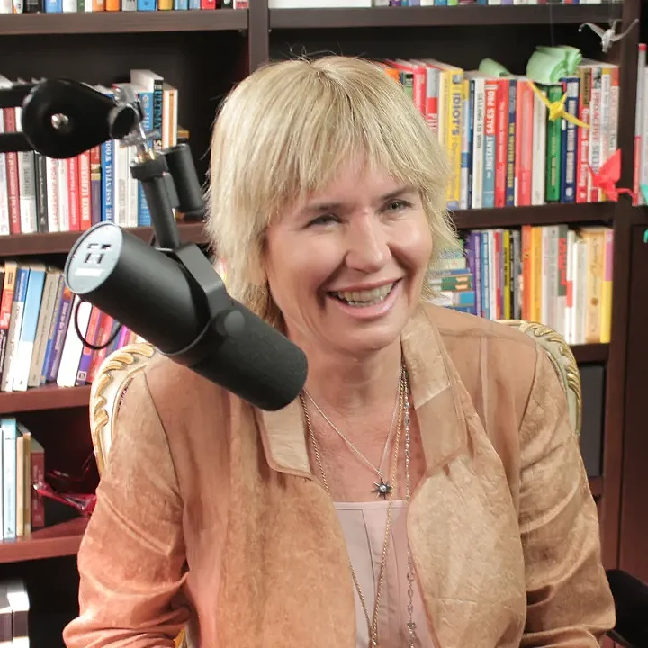 Remi smiling at a podcast microphone in front of a wall of books